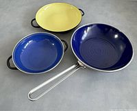 Yellow and blue double-handled enamelled pans with blue frying pan showing circular ridged base and long metal handle.