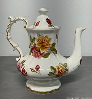 Side view of teapot showing bulbous body with pink and yellow roses and gold trimmed handle and spout