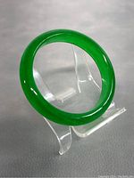 Green jade bangle placed on clear plastic stand, showing the smooth and polished surface of the bangle.