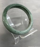 Close-up side view of the natural green jade bangle on a clear stand showing color and polish.