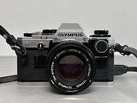 Front view of Olympus OM10 35mm film camera showing lens and manual adapter label on right side of mount.