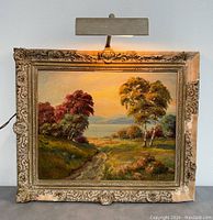Full view of framed oil landscape painting with wall light above, showing frame damage and visible brushwork.