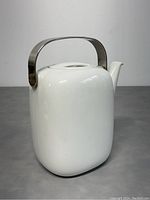 Front view of the white porcelain teapot showing square rounded shape and metal handle
