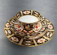 Photo of trio set stacked with tea cup, saucer and plate showing floral and black background pattern with gold accents