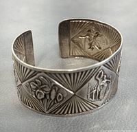 Close-up photo of the silver cuff bracelet showing embossed designs and open back.