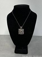 Front view of sterling silver pendant necklace displayed on black bust, showing rectangular pendant with scroll filigree design and chain.