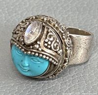 Front angle showing carved turquoise face, ornate filigree crown with moonstone, and bent ring band