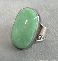 Close-up angled view of sterling silver ring with large oval green stone on textured grey surface