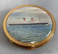 Top view of compact showing gold-tone outer edge and printed image of R.M.S. Queen Elizabeth ship on lid.