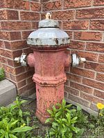 Full side view of the antique red and white fire hydrant placed against a brick wall corner, showing weathered paint and cast iron structure.