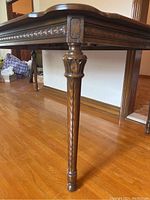 Close-up of the carved, fluted legs and decorative apron edge of the walnut dining table.