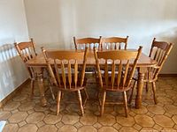 Dining table with leaf extended and six matching chairs arranged around it on a tiled floor.