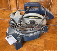 Angle view showing the full Mastercraft mitre saw with power cord coiled on top, mounted on a base with angle settings.