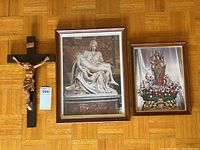 Photo of crucifix with dark wood cross and two framed religious prints on wood floor.