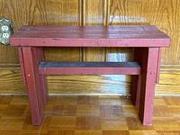 Vintage rustic wooden bench painted red, front view showing sturdy legs and horizontal support beam.