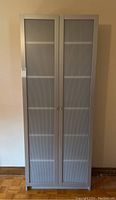 Front view of the tall grey IKEA cabinet with closed double doors showing plastic panel surfaces and small handles.