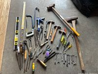 Wide view of the entire collection of assorted hand tools including woodworking files, hammers, caulking gun, and various other small hand tools arranged on concrete floor.