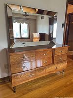 Front view of the vintage wood grain low dresser with six drawers and brass leaf-shaped drawer pulls, and large beveled mirror above it not attached.