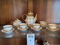 Full tea set arranged on a glass shelf showing all items: teapot, sugar bowl, 5 cups, and 5 saucers.