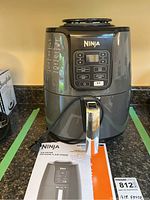 Front view of Ninja air fryer with digital control panel and stainless steel handle. Included instruction manual visible.