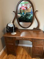 Front view of dresser with attached oval mirror, desk lamp and desk fan on top