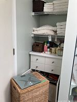 View of closet shelves with folded white towels and bathrobe, and brown wicker baskets