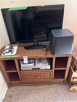 Rattan corner cabinet holding LG 32-inch TV, Polk Audio subwoofer speaker on top, and Samsung DVD/VHS combo player inside.