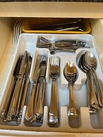 Photo showing organized stainless steel cutlery with knives, forks, and spoons in plastic tray and yellow basket.