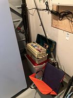 Fishing rod, tackle box filled with fishing gear, cooler beneath, and padded seat cushion stacked beside.