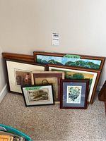 Six framed artworks leaning against a wall on carpet, showing different frame styles and sizes.