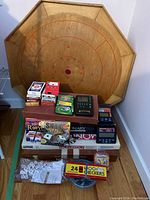 Wide view of assorted games including wooden game board, boxed board games, playing cards, electronic games, dice, and checkers set in yellow box.