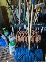 Wide shot of garden tools including shovels, rakes, broom, garden edging and storage rack in shed environment