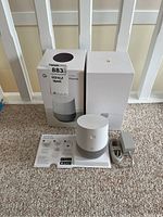 Google Home smart speaker with original box, power adapter, and user manual arranged on carpeted floor