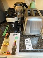 Full view of Ninja blender with base, blending cup, blade assembly, and instruction manual alongside toaster and electric kettle on countertop.