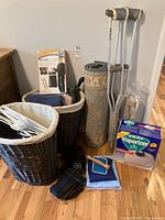 Full lot showing two wicker laundry baskets, towels, clothes hangers, rolled rug, crutches, knee brace, vaporizer box, and Space Hanger box.