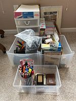 Clear plastic storage containers filled with assorted office supplies and paper products on carpet.