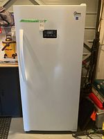 Front view of white upright freezer with handle, digital display, and Midea logo in basement setting.