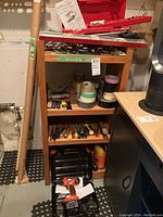 Wooden cabinet holding assorted hand tools, screwdrivers, wrenches, rolls of tape, and other equipment with a hand saw resting nearby in basement setting.