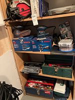 Shelving unit with Bosch random orbit sander, finishing sander on their boxes, various toolbox sets, and accessories including rotary mower tool sharpener and sand blades