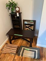Wooden cabinet, wooden bench, wooden framed mirror, three small rugs, and clock displayed together in a corner with hardwood floor.
