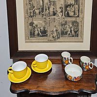 Photo showing two yellow Arzberg cups with matching saucers, two white floral Acapulco mugs, and one Acapulco bowl with a matching floral design.