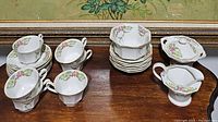 Photo showing 6 teacups, 6 saucers, 6 small bowls, 1 cream pitcher, 1 sugar dish, and 1 dish arranged on a wooden surface.