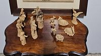 Full view of all nativity scene figurines arranged on wooden surface including humans and animals in natural clay color.