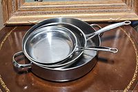 Three stainless steel pans stacked with two skillets and one larger pan with handles below