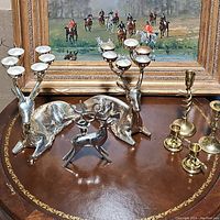 Overview of all candlestick holders arranged on a decorative table, showing three silver reindeer-shaped holders and four brass candlestick holders.
