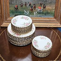 Stacked dinner, salad, and bread plates displaying the floral pink rose pattern with gold trim.