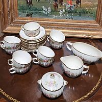 Photo showing 6 teacups stacked alongside 12 saucers stacked with a gravy boat, a creamer pitcher, and a sugar dish with lid in matching China Rose pattern with 22k gold trim.