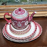 Top-down photo showing the vintage teapot centered on stacked plates featuring the Mandarin Maroon pattern with gold details on the china pieces.