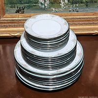 Stack of Noritake Greenbrier china plates showing multiple sizes consistent with dinner, dessert, and bread plates, stacked neatly to display quantity and pattern details.