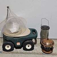 Step 2 garden cart with three different bird feeders placed on and beside it.